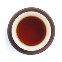 Brewed deep red Dian Hong tea liquor in a white porcelain cup on a clay coaster, seen from above