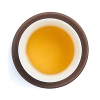 Brewed golden green tea liquor in a white porcelain cup on a clay coaster, seen from above