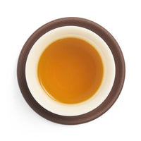 Brewed golden amber oolong tea liquor in a white porcelain cup on a clay coaster, seen from above