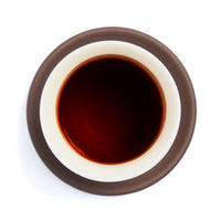 Brewed dark aged oolong tea liquor in a white porcelain cup on a clay coaster, seen from above