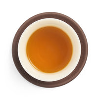 Brewed rich golden amber oolong tea liquor in a white porcelain cup on a clay coaster, seen from above