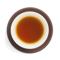 Brewed amber sheng puerh tea liquor in a white porcelain cup on a clay coaster, seen from above