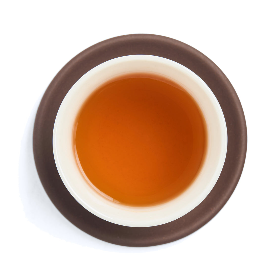 Brewed amber-orange black tea (heicha) liquor in a white porcelain cup on a clay coaster, seen from above