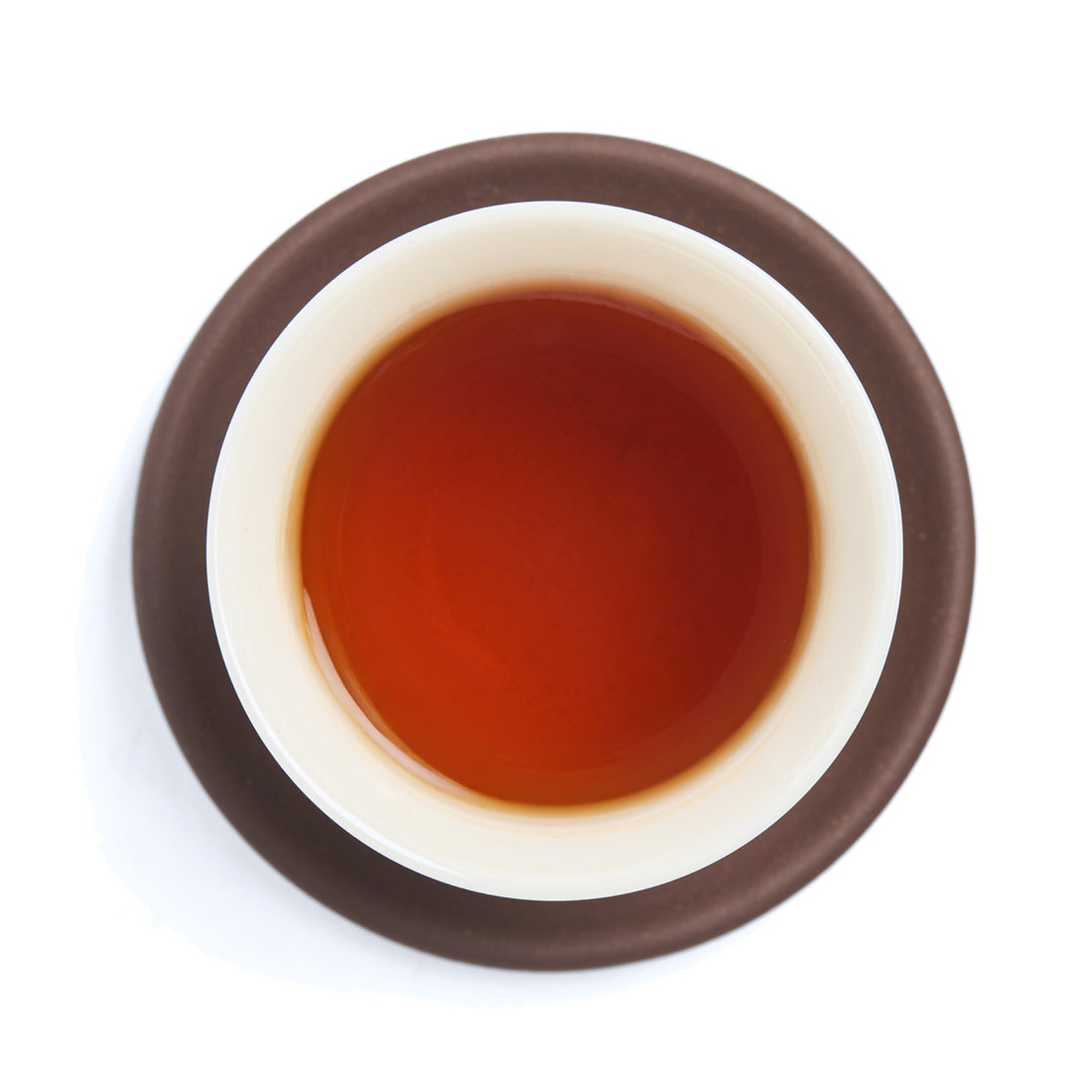 Brewed red-amber black tea (heicha) liquor in a white porcelain cup on a clay coaster, seen from above