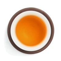 Brewed amber herbal tea blend liquor in a white porcelain cup on a clay coaster, seen from above