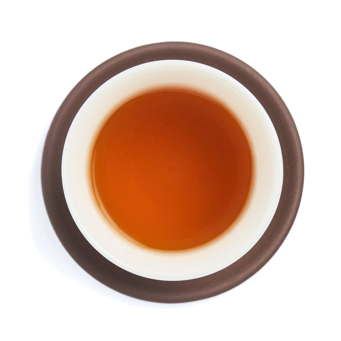 Brewed amber-red Dian Hong tea liquor in a white porcelain cup on a clay coaster, seen from above