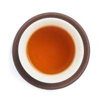 Brewed amber-red Dian Hong tea liquor in a white porcelain cup on a clay coaster, seen from above