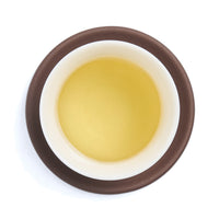 Brewed pale green tea liquor in a white porcelain cup on a clay coaster, seen from above