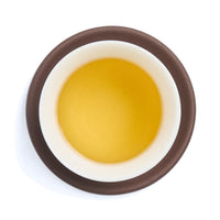 Brewed pale golden oolong tea liquor in a white porcelain cup on a clay coaster, seen from above