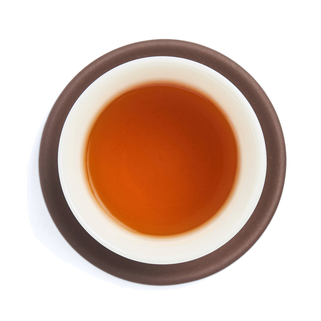 Brewed deep amber oolong tea liquor in a white porcelain cup on a clay coaster, seen from above