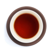 Brewed deep red tea liquor in a white porcelain cup on a clay coaster, seen from above