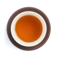 Brewed amber red tea liquor in a white porcelain cup on a clay coaster, seen from above