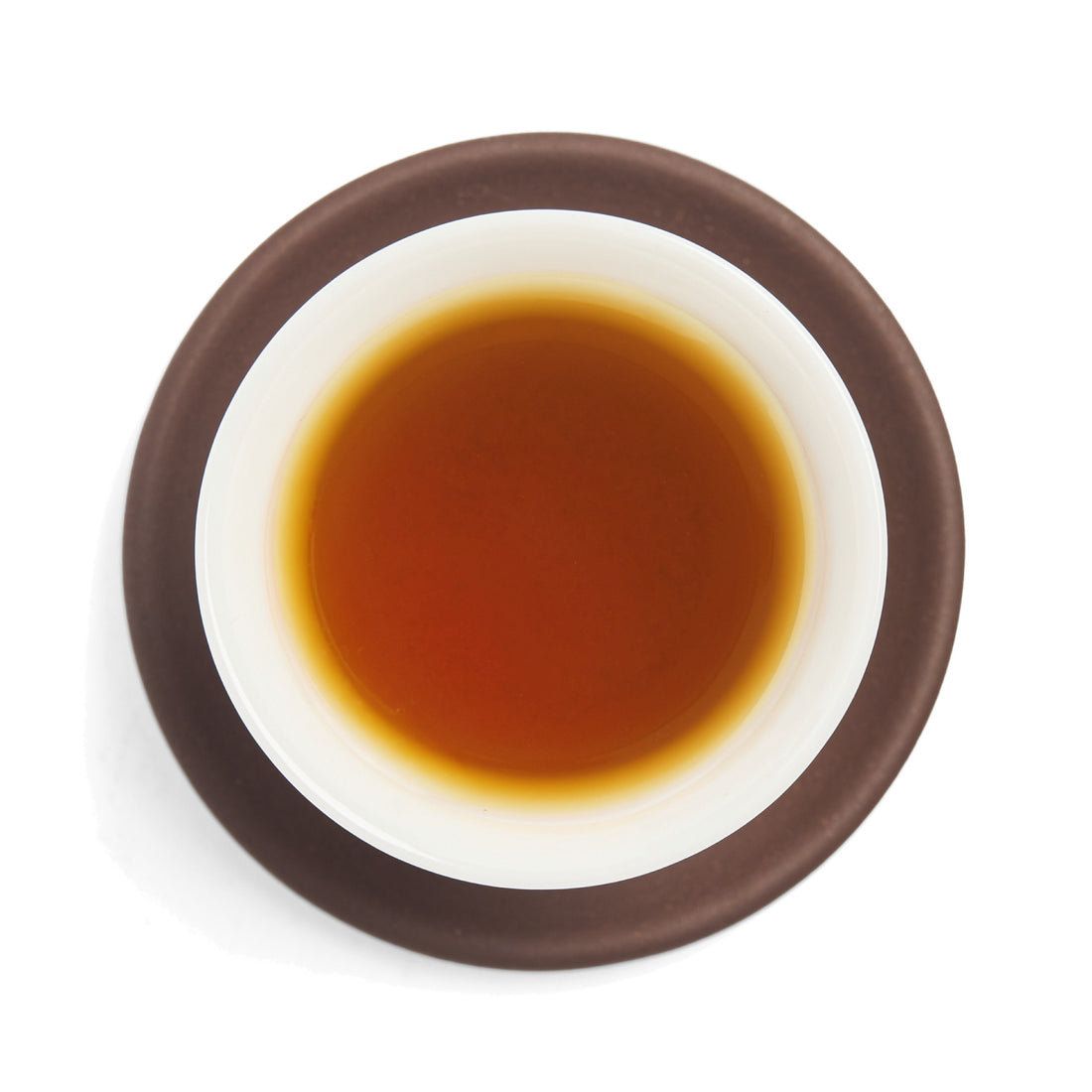 Brewed amber sheng puerh tea liquor in a white porcelain cup on a clay coaster, seen from above