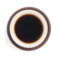 Brewed dark aged sheng puerh tea liquor in a white porcelain cup on a clay coaster, seen from above