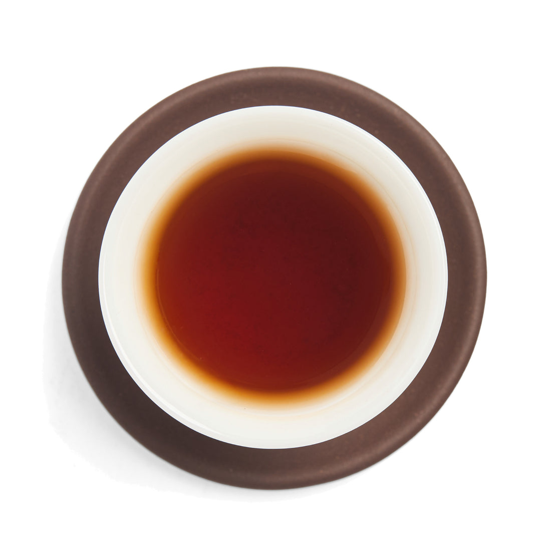 Brewed deep red sheng puerh tea liquor in a white porcelain cup on a clay coaster, seen from above