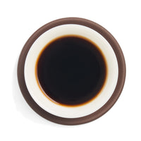 Brewed shou puerh tea liquor in a white porcelain cup on a clay coaster, seen from above