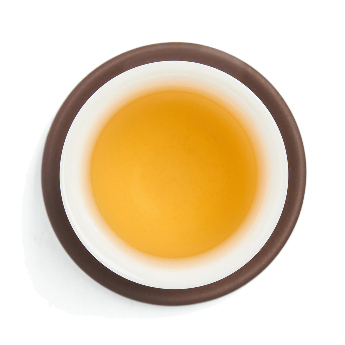 Brewed pale golden white tea liquor in a white porcelain cup on a clay coaster, seen from above